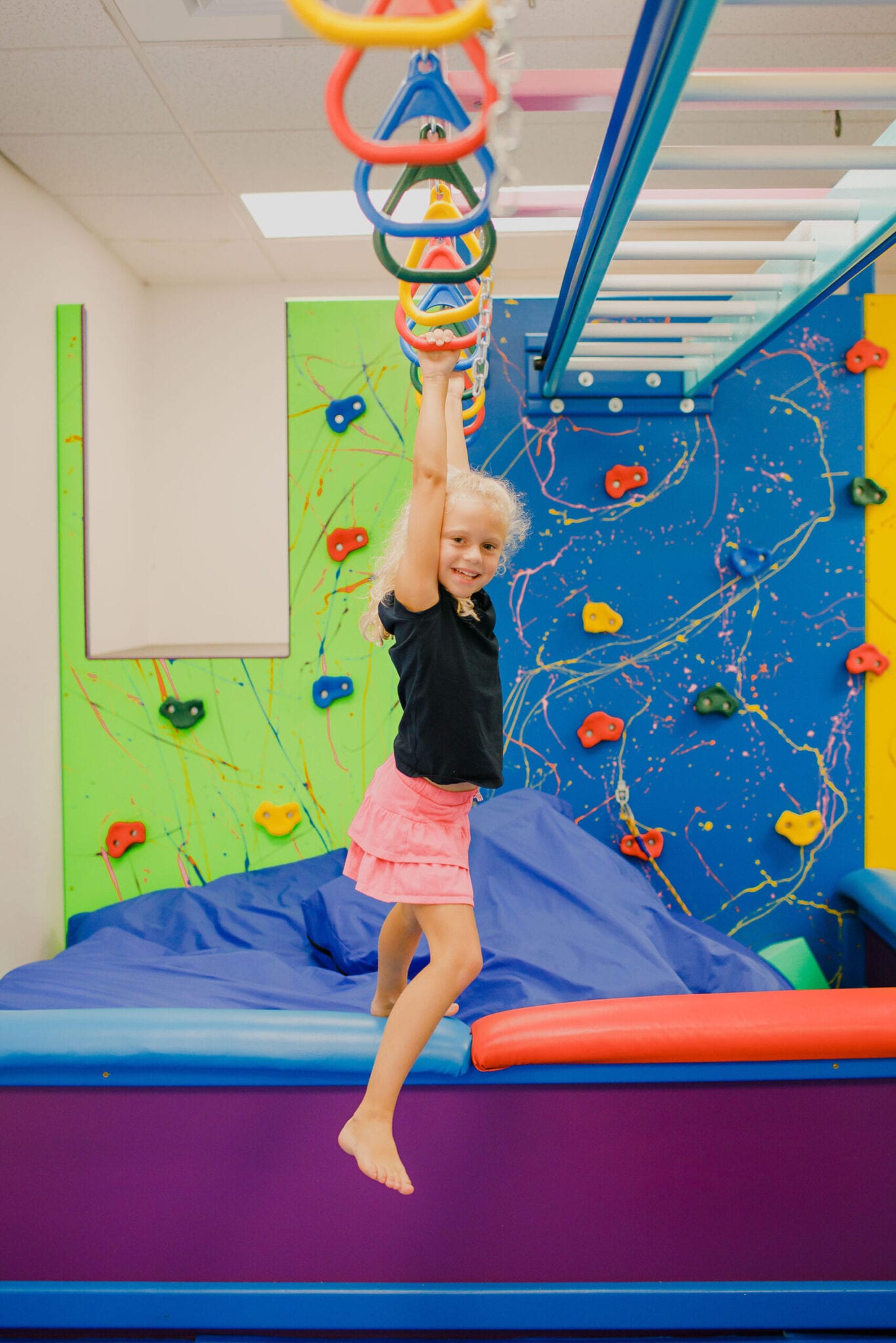 Niña columpiándose en las barras de mono en el Sensory Gym