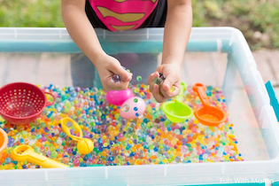 Un niño jugando en un contenedor sensorial lleno de perlas de agua y juguetes