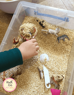 Mano de niño jugando en un contenedor sensorial lleno de avena y juguetes